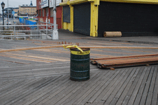 The Coney Island boardwalk, with amusements and stores on the right and a fence surrounding an area under repair.